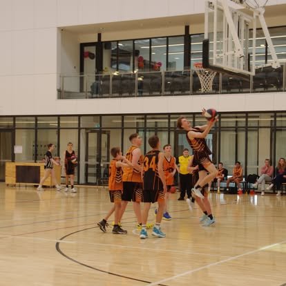 A Panthers junior boys team in orange and black singlets during a game at MARC Stadium, one player driving to the basket as teammates and opponents close in.